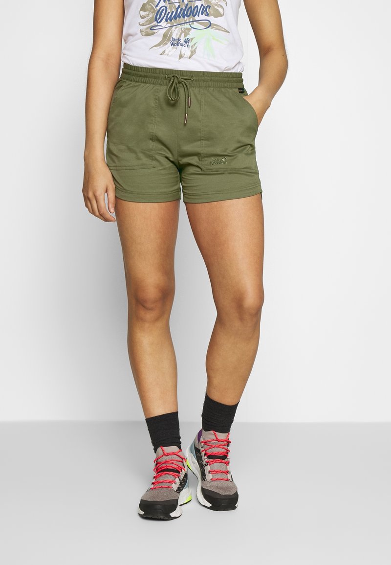 Kaki gröna shorts med elastisk midja, sidofickor och broderad logotyp. Matchas med grå sneakers med ljusa snörningar och mörka strumpor.