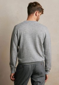 Jasnoszary sweter z dzianiny z okrągłym dekoltem i ściągaczami, noszony na ciemnoszarych spodniach, prezentujący gładką teksturę i swobodny krój.