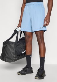 Ανοιχτό μπλε αθλητικά σόρτς με ελαστική μέση και ένα μικρό μαύρο λογότυπο Nike. Μαύρη τσάντα duffel Nike, κάλτσες και μαύρα αθλητικά παπούτσια.