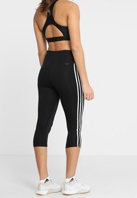 Černé sportovní crop legíny s bílými bočními pruhy, vysokým pasem a hladkým, elastickým materiálem. Sportovní podprsenka s vykrojeným zadním dílem.