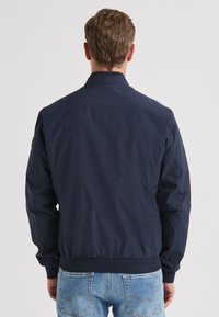 Marineblaue Bomberjacke mit glattem Stofffinish, gerippten Bündchen und Bund. Verfügt über einen Stehkragen und ein schlichtes Design.
