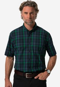 Camicia a maniche corte a quadri nei colori blu scuro e verde. Presenta un colletto, chiusura con bottoni e una vestibilità comoda. Indossata con una cintura marrone e pantaloni scuri.