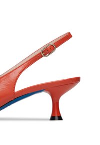 Scarpa slingback rossa in pelle con una fibbia decorativa e un tacco a cono unico. La base presenta dettagli blu e un punta nera.