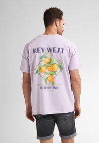 Fialové bavlněné tričko s grafikou pomerančů a listoví, s textem "KEY-WEST" a logem značky. Krátké rukávy, uvolněný střih.