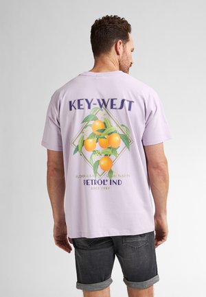 Camiseta de algodón morada con un gráfico de naranjas y follaje, con el texto "KEY-WEST" y el logo de la marca. Mangas cortas, corte relajado.