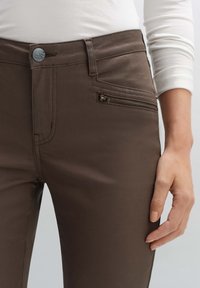 Vihreät housut, jotka on valmistettu pehmeästä kankaasta, jossa on etutasku vetoketjulla. Ominaisuuksiin kuuluu metallipainike suljettuna ja hienovaraiset ompeluyksityiskohdat.