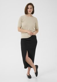 Haut crème à pois avec un col rond, associé à une jupe en denim noire avec une fente sur le côté et des ballerines noires avec un détail en nœud.