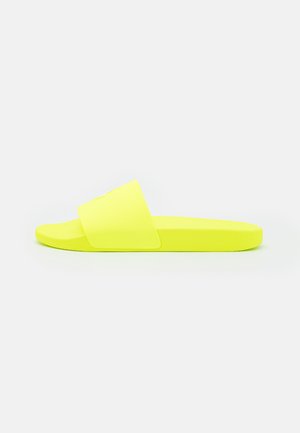 Sandale slip-on jaune vif avec une large sangle et une semelle plate, présentée de profil sur un fond blanc uni.