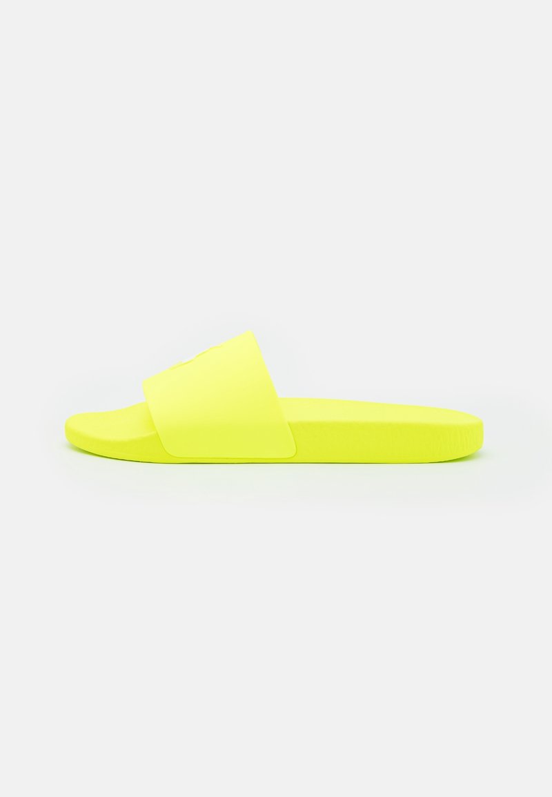 Sandale slip-on jaune vif avec une large sangle et une semelle plate, présentée de profil sur un fond blanc uni.