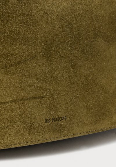 Grønne ruskindmateriale med en glat tekstur og fin korn. Har et trykt logo "REE PROJECTS" nær bunden. Enkel design.