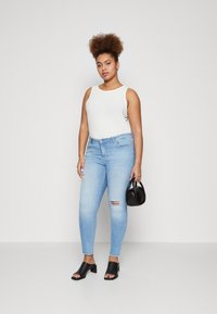 Šviesiai pilkas rankovių tankas, šviesiai mėlyni siauri džinsai su suplėšytais keliais, juodos atviros pirštinės kulniuko mules, ir mažas juodas rankinukas. Minkšta tekstūra.