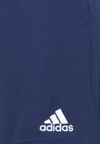 Shorts de sport bleu marine en tissu doux, présentant un logo Adidas brodé blanc en bas à gauche. Texture lisse, design simple.