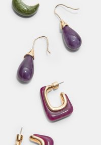 Lilla dråbeøreringe med gulddetaljer, en grøn halvmåneørering og en lyserød geometrisk hoop-ørering, alle med blanke overflader.