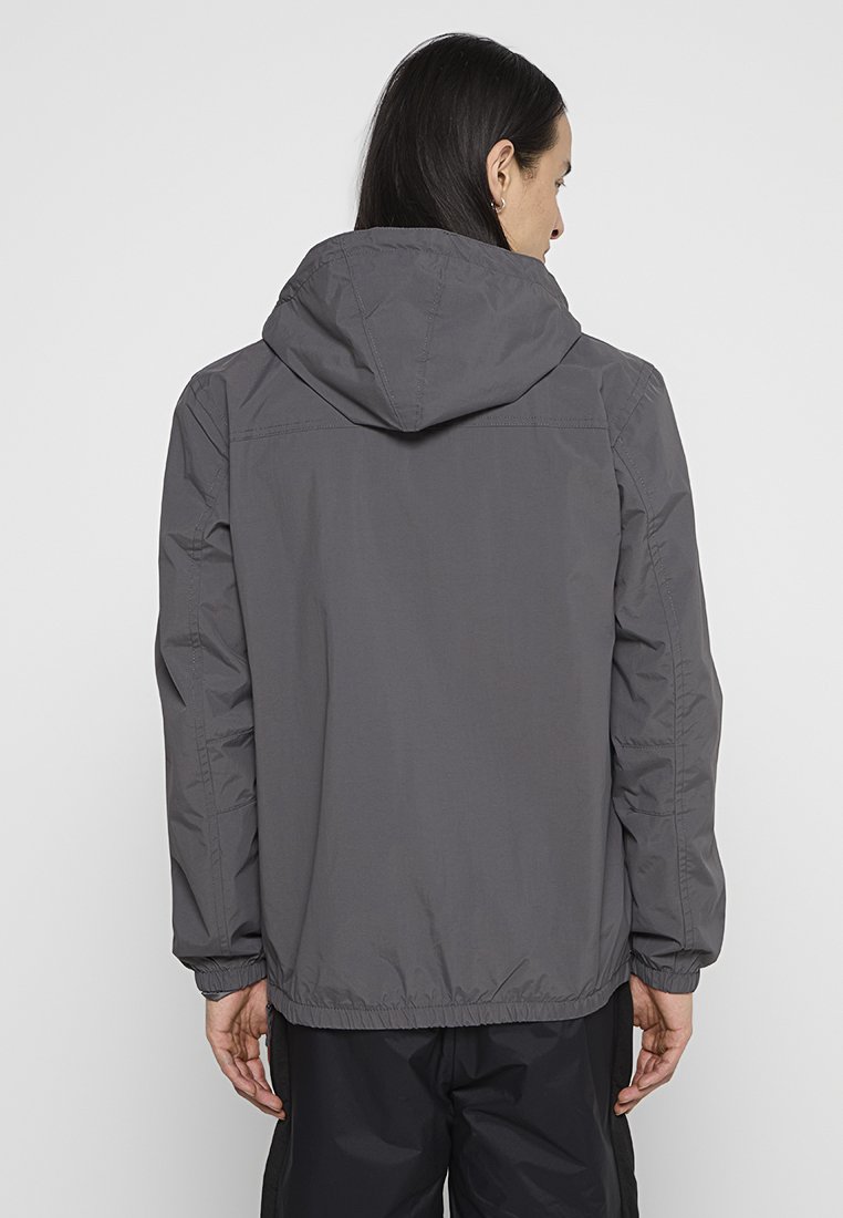 Szara kurtka z kapturem, z elastycznymi mankietami i dołem, o gładkiej, matowej fakturze i prostym designie. Widok z tyłu.