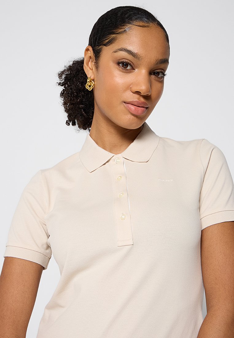 Cremfarbener Poloshirt mit strukturiertem Finish, klassischem Kragen, kurzen Ärmeln und einer Fünf-Knopf-Leiste. Dezente Markenkennzeichnung auf der Brust.