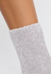 Grau fuzzy Socke mit einer weichen Textur und einem plüschigen Bündchen. Die Socke bedeckt einen Teil eines nackten Beins und hebt das gemütliche Design hervor.