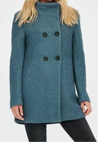 Cappotto in misto lana di colore turchese con colletto alto, chiusura a doppio petto con bottoni e due tasche laterali. Tessuto morbido con leggeri riflessi.