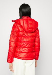 Röd puffjacka med avtagbar huva, kviltat mönster och glänsande yta. Har långa ärmar och justerbar nederkant.