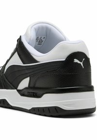 Shoe sportiv alb-negru cu un superior din piele texturată, guler căptușit și talpă din cauciuc. Prezintă un logo Puma proeminent pe călcâi.