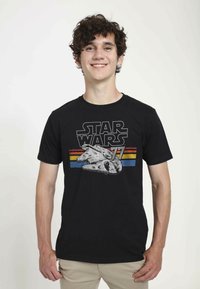 Černé bavlněné tričko s grafikou Millennium Falcon a textem "STAR WARS" spolu s barevnými vodorovnými pruhy v modré a žluté barvě.