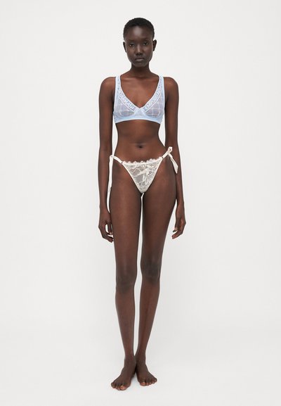 Bralette in pizzo blu chiaro con motivi floreali, abbinato a un perizoma bianco in pizzo con lacci laterali; tessuto trasparente e delicato.