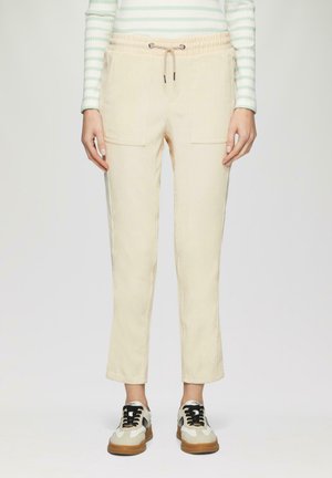 Lichtbeige broek met een elastische tailleband en trekkoord, voorzien van twee voorzakken en een toelopend pijpontwerp.