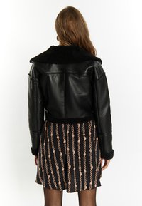 Sort læder cropped jakke med shearling krave og manchetter, parret med et mønstret nederdel med guld- og pink kædemotiver.