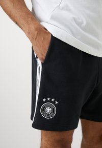 Calções de algodão pretos com riscas laterais brancas e um logotipo circular com uma águia e cinco estrelas na parte inferior da perna.