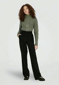 Zaļš rievots augstais kakls džemperis ar kabelīša adījuma rakstu, apvienots ar melniem augstiem biksēm. Rādas platās kājas un elegants siluets.