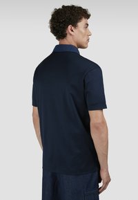 Polo shirt blu navy con colletto classico, maniche corte, texture liscia e design posteriore che presenta un colletto a contrasto discreto.