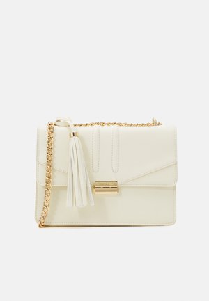 Sac à main en cuir crème avec une chaîne en or, un pompon à l'avant et un fermoir rectangulaire en or avec le nom de la marque.