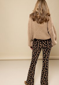 Beige brei sweater met een loose fit, gecombineerd met zwarte flared pants met een bloemenpatroon in roze en geel. Neutrale schoenen maken de look compleet.