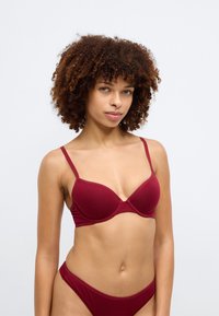 Μπραζίνα μπορντό με λεπτές τιράντες, υποστήριξη με μπανέλα και απαλό, ελαστικό ύφασμα. Διαθέτει διακριτική ραφή κατά μήκος των cups.