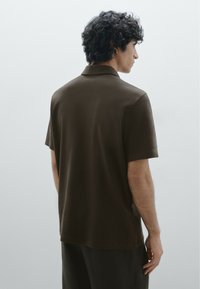 Polo shirt marrone con una texture morbida, maniche corte e colletto classico. La vista da dietro mette in evidenza una vestibilità rilassata e linee pulite.