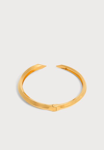 Bracelet manchette en or brillant ouvert avec une finition lisse, présenté sur une surface grise claire.