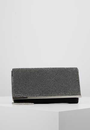Pochette rectangulaire noire avec des strass argentés, une bordure métallique et une bandoulière chaîne argentée reposant sur une surface blanche.