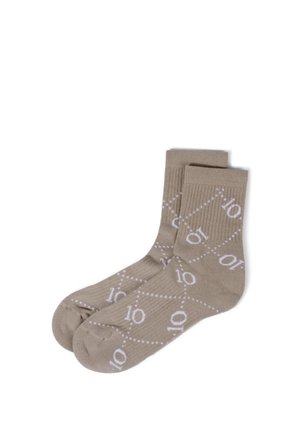 Chaussettes basses marron clair à lignes diagonales blanches en pointillés et motif "10" répété, posées à plat côte à côte sur fond blanc.