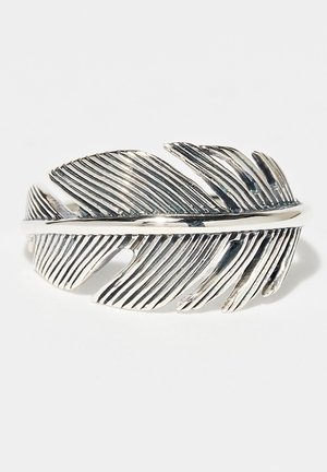 Bague en argent en forme de plume détaillée avec des rainures texturées et des sections ajourées, présentée sur un fond blanc.