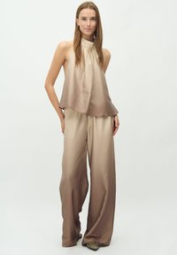 Top senza maniche con collo alto in una gradazione di beige chiaro a scuro, abbinato a pantaloni a gamba larga in tonalità coordinate. Realizzato in tessuto morbido.