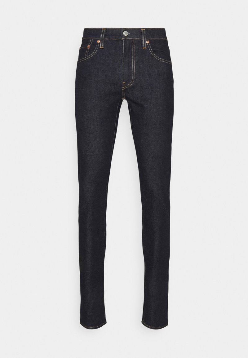 Jeans skinny em denim escuro com detalhes em cobre, cinco bolsos, costuras em destaque e um design de cintura clássica.