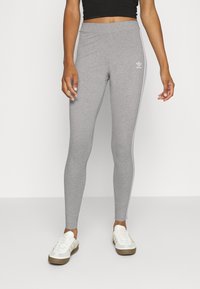 Grå leggings gjorda av mjukt material, åtsittande design med vita sidostraper, med en Adidas-logotyp på övre låret.
