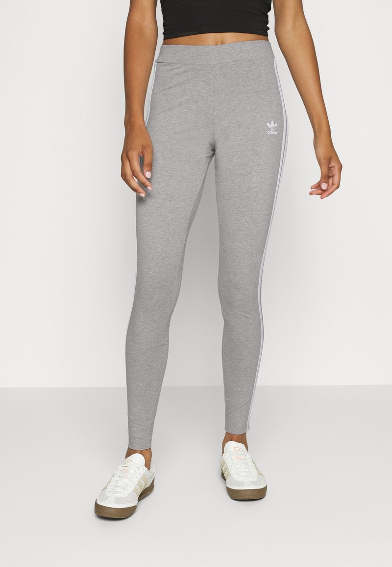 Grå leggings gjorda av mjukt material, åtsittande design med vita sidostraper, med en Adidas-logotyp på övre låret.