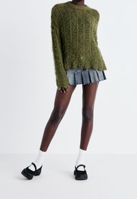 Grüner, flauschiger Strickpullover mit geripptem Muster, kombiniert mit einem aus Jeansstoff gefalteten Minirock und schwarzen Plateauschuhen mit Knöchelriemen.