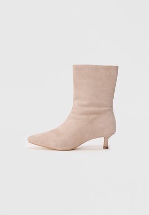 Beige suede ankle boot with a pointed toe and a low kitten heel. Smooth texture with a sleek silhouette and minimalistic design.