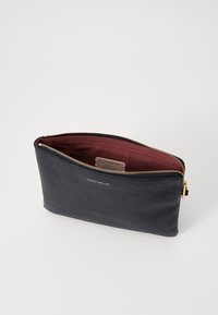 Pochette en cuir noir avec une finition texturée, fermeture éclair dorée et intérieur bordeaux. Comprend une étiquette logo visible à l'intérieur de la pochette.