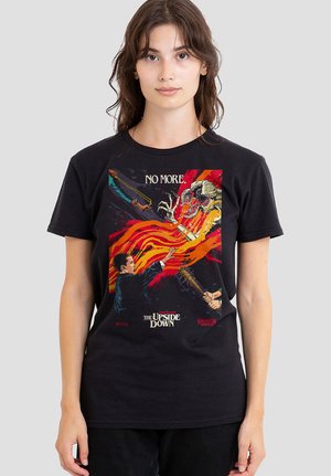 Young woman wearing a black Stranger Things T-shirt showing characters fighting the Demogorgon with fire and weapons.