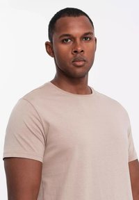 Beżowa bawełniana koszulka z okrągłym dekoltem, krótkimi rękawami i gładką teksturą. Prosty design bez widocznych wzorów czy akcentów.