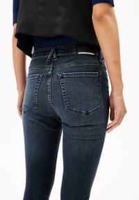 Mörkblå denimjeans med slim fit, som har två bakfickor och en midjebandsetikett. Tyget har en slät, något urtvättad struktur.
