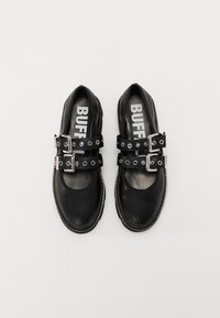 Zapatos de cuero negro con doble hebilla, herrajes plateados y acentos de tachuelas circulares; con puntera redondeada y un interior acolchado.