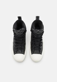 Svarta högskurna sneakers med en texturerad ovandel, vit gummitå, och kontrasterande sömmar. Har en vadderad svart krage och snören.